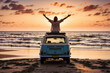 A person sits on top of a classic van with arms raised, enjoying the freedom and beauty of a vibrant sunset over the ocean. A hippie lifestyle concept.