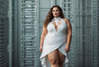 A confident plus size model poses in a white bodycon dress with revealing cutouts, showcasing body positivity in an urban setting.