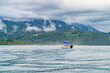 Leisure boat cruising on a serene sea with a misty mountainous backdrop and lush tropical forests. Tranquil ocean waters before a tropical coastline with clouds descending upon verdant hills. High