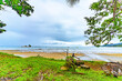 Serene tropical beach scene with overcast skies, framed by verdant foliage and a view of distant islands. High quality photo. Uvita Puntarenas Province Costa Rica
