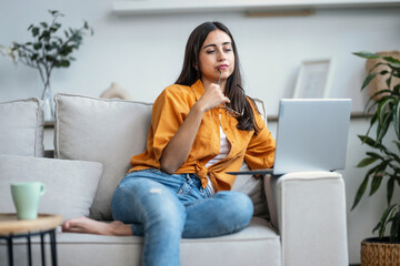 Wall Mural - Pretty young woman working with her laptop while sitting on couch at home.