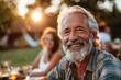 An elderly man with a white beard smiles warmly at an outdoor dinner during golden hour