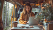 © Raquel - Woman working with her laptop on the table, next to her cell phone and coffee, in a yellow camper van