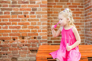 Child blowing soap bubbles with cochlear implant system. Installation cochlear implant on child girl ear for restores hearing. Kid hears after hear return to normal. Diversity inclusion concept. Copy