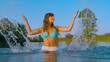 PORTRAIT: Attractive young woman in bikini stands in river and splashes water