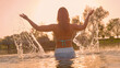 LENS FLARE: Young female in a swimsuit gracefully raises arms and splashes water