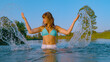 PORTRAIT Beautiful woman in bikini stands waist deep in river and splashes water
