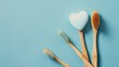 Three wooden toothbrushes are arranged in a row on a blue background. The toothbrushes are of different colors and sizes, and they are placed in a way that they form a heart shape