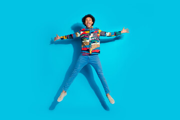 Poster - Full length photo of handsome young guy jumping spread legs hands dressed stylish print garment isolated on blue color background