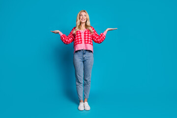 Sticker - Full size photo of adorable person dressed knitwear jumper jeans look at product on arm empty space isolated on blue color background