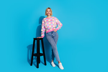 Poster - Full length photo of lovely girl wear checkered pullover pants lean on bar chair hold palm in pocket isolated on blue color background