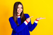 Photo portrait of pretty teen girl hold point empty space wear trendy knitwear blue outfit isolated on yellow color background