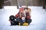 Fototapeta Dmuchawce - Dziewczyna siedzi na śniegu z trzema psami: pekińczykiem, czarnym kundelkiem i chihuahua