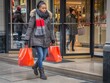 Foto de uma mulher saindo de uma loja com sacolas de compras na mão, capturando o conceito de compras e consumo