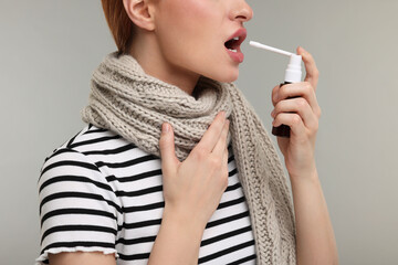 Canvas Print - Young woman with scarf using throat spray on grey background, closeup