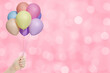 Female hand holds bunch of colorful balloons on pink blurred background. Empty space for text