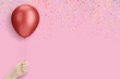 Female hand holding the red balloon on pink background with confetti. Empty space for text
