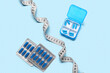 Container, blister packs with weight loss pills and measuring tape on blue background