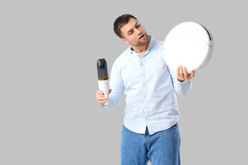 Wall Mural - Handsome man with handy and robot vacuum cleaners on light background