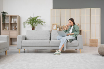 Canvas Print - Pretty young woman with laptop sitting on grey sofa in living room