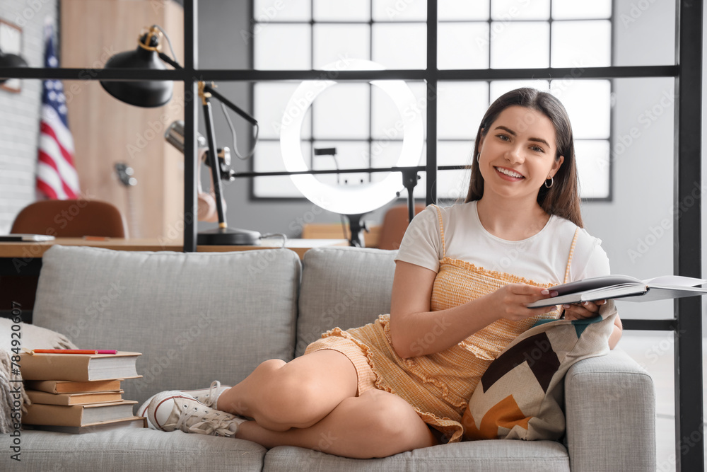 Female student reading book on sofa at home