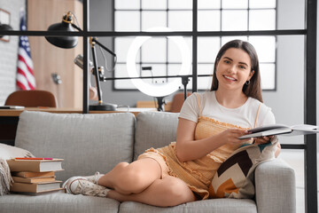 Wall Mural - Female student reading book on sofa at home