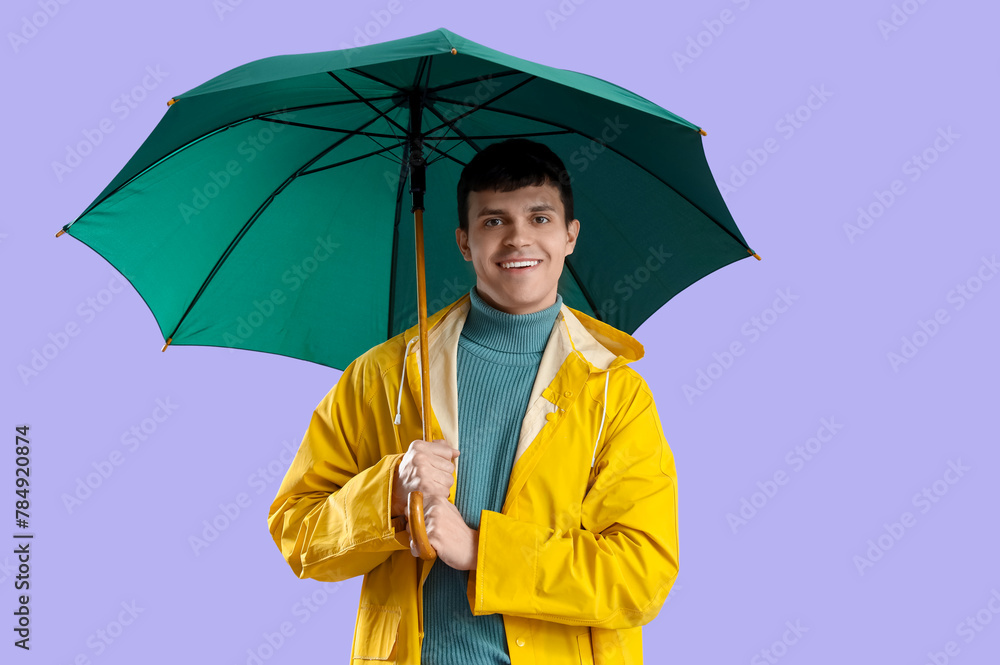 Young man in raincoat with green umbrella on lilac background