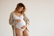 © looking2thesky - A beautiful pregnant girl in a white bodysuit and an oversized jacket, wavy hair. A pregnant beauty is expecting the birth of a child. Clothes for pregnant women, copy space. Motherhood and Childhood