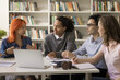 © fizkes - Pretty red-haired schoolgirl talk to diverse schoolmates met in campus library. Group of interracial students listen team leader, express opinion, solution, ideas, studying together on joint project