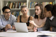 © fizkes - Four focused multiethnic students do homework together sit in library, discuss online task use laptop, prepare for exams, search information on internet, share ideas, work on group project. Education
