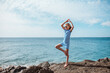 Young girl standing on one leg on rock. Blonde girl in dress enjoying vacation in Canary Islands. Concept of beach summer vacation with kids.