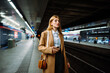 © Big Shot Theory - Female standing at subway platform with mobile phone, using social media and waiting train
