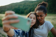 © Halfpoint - Young teenager girl best friends spending time in nature, during sunset. Girls on walk, taking selfie with smartphone.