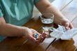 © Westend61 - Woman holding capsules in hand by glass of water on table at home