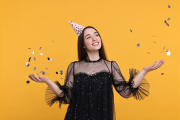 Canvas Print - Happy woman in party hat throwing confetti on orange background