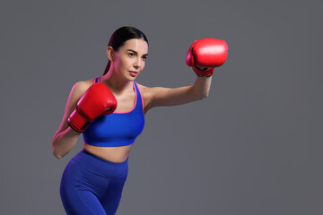 Poster - Beautiful woman wearing boxing gloves training in color lights on grey background