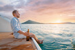Holiday on the sea. Relaxed young man with beer bottle sitting on the yacht deck on sunset