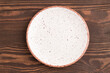 Empty white ceramic plate on brown wooden background. Top view, copy space