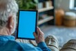 Digital mockup over a shoulder of a elderly man holding an ebook with an entirely blue screen