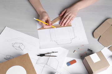 Woman creating packaging design at light wooden table, top view