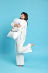 Wall Mural - Happy woman in pyjama holding pillow on light blue background