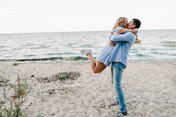 Couple in love hugging and kissing each other on seashore. Man and woman standing on sand sea. Side view. Female and male kisses on beach ocean and enjoying sunny summer day. Spending time together