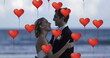 Image of multiple red heart balloons floating over newly married couple embracing on beach