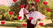 Image of multiple red heart balloons floating over newly married couple groom carrying his bride