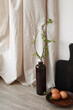 Elegant sustainable rustic Easter kitchen interior, natural color eggs on brown ceramic plate, vase with green tree branch on table, beige linen curtain, empty white wall with soft sunlight shadows.
