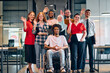 © .shock - A diverse group of young business people walking a corridor in the glass-enclosed office of a modern startup, including a person in a wheelchair and a woman wearing a hijab