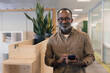 © ReeldealHD images - Portrait of a successful African american mature adult businessman in an office holding his cell phone