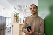 © ReeldealHD images - Portrait of a new employee in a modern corporate office holding a smartphone