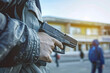 Close up of young man with a pistol gun standing in front of a high school building in blurry background