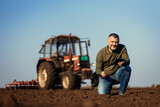 Fototapeta Zachód słońca - Portrait of satisfied mature farmer standing in field with tablet supervises the cultivation of soil.